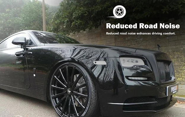 Luxury black Rolls-Royce parked on a quiet road, featuring large custom black wheels with a thin-spoke design. Text overlay reads “Reduced Road Noise – Reduced road noise enhances driving comfort,” accompanied by a tire icon.