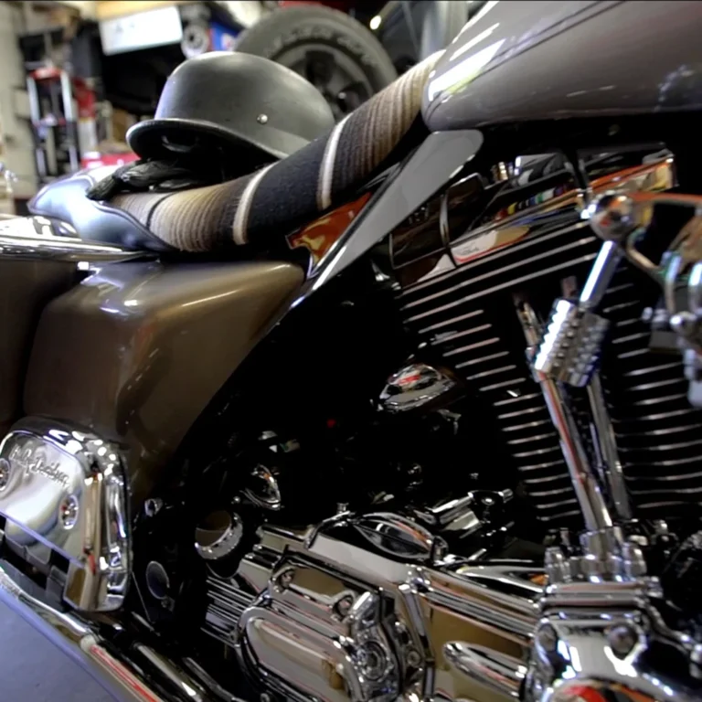 Close-up side view of a Harley-Davidson motorcycle with a brown and chrome finish, featuring a striped blanket seat cover and a black half-helmet resting on the seat. The polished engine components reflect the workshop surroundings.