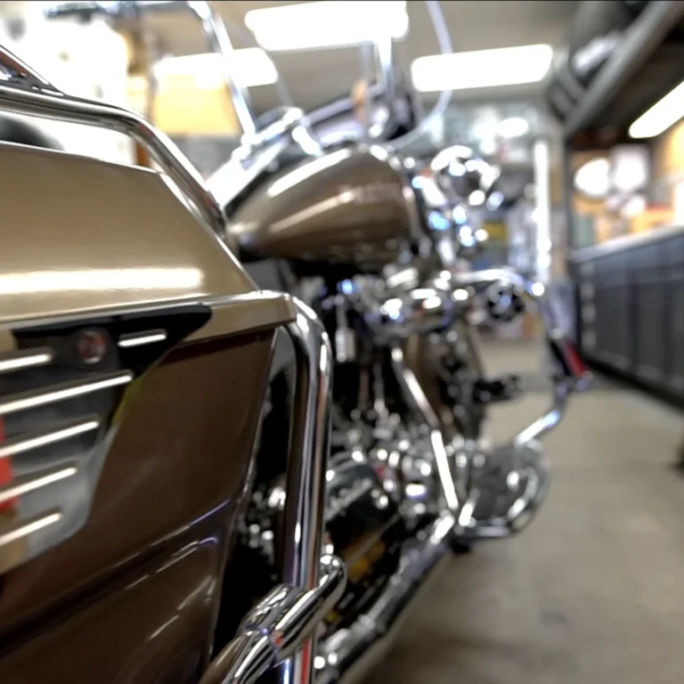 Close-up of a metallic brown touring motorcycle with chrome detailing, captured indoors in a workshop or garage. The foreground highlights protective chrome bars and side fairing, with the rest of the bike softly blurred in the background.