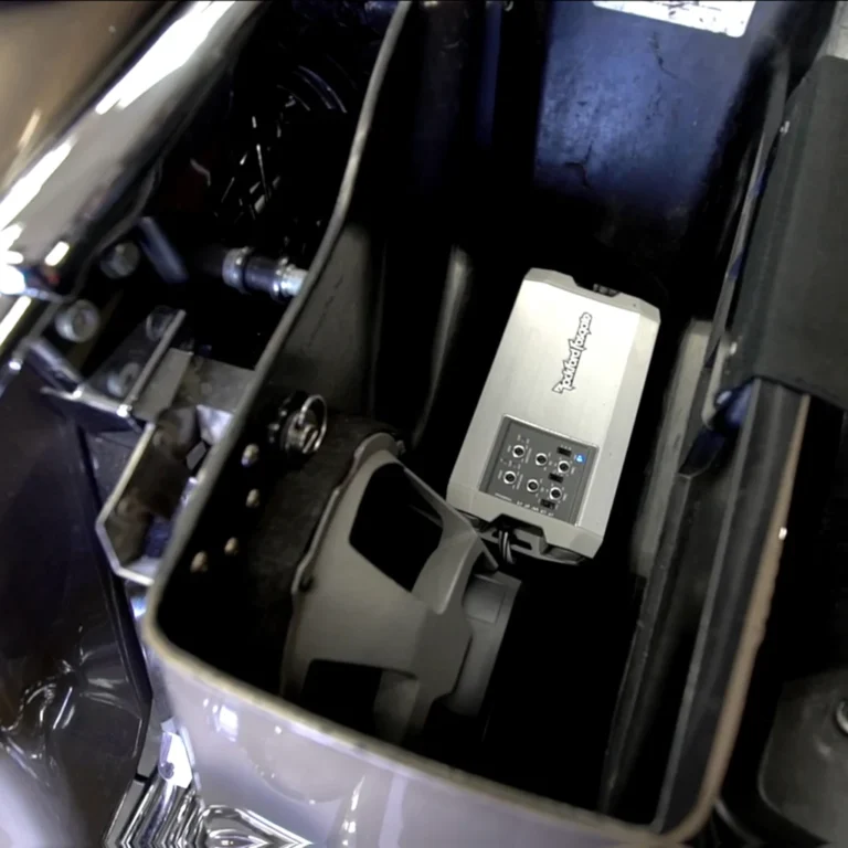 Interior view of a motorcycle saddlebag housing a Rockford Fosgate audio amplifier and a mounted speaker, part of a custom sound system installation with visible wiring and mounting hardware.