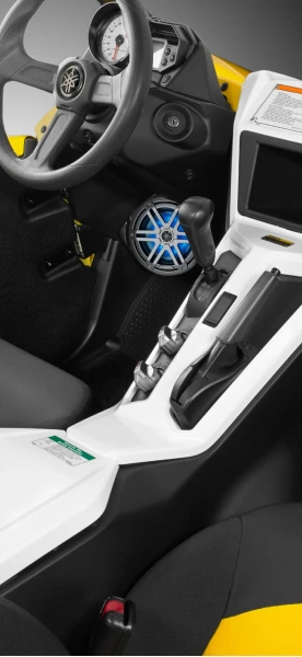 Interior of a Yamaha side-by-side or ATV with a blue marine-grade speaker installed near the gear shift and a detailed view of the steering wheel, dashboard, and infotainment screen.