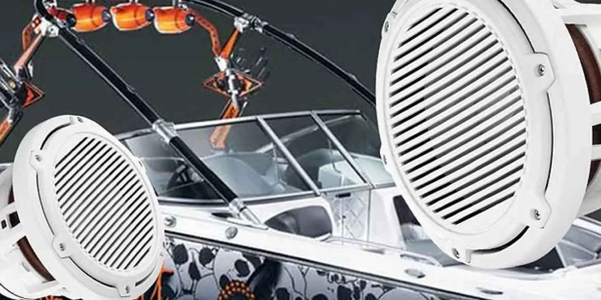 Close-up image of two large white marine speakers superimposed over a customized wakeboard boat with tower-mounted orange speakers and a sleek, patterned hull design.