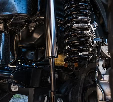 Close-up view of a vehicle’s suspension system showing a heavy-duty coil spring, shock absorber, and various metal components, highlighting an upgraded off-road or performance suspension setup.
