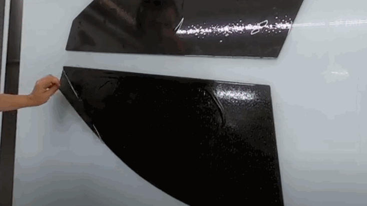 Hands carefully peel a precut window tint piece from a white backing sheet, ready to be installed onto a car window.