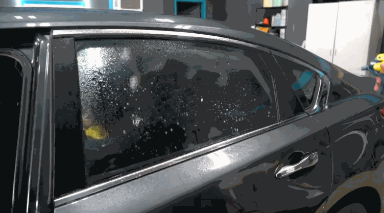 Technician sprays solution on a car’s rear window before smoothing out a tinted film, prepping the surface for a clean and secure tint application.