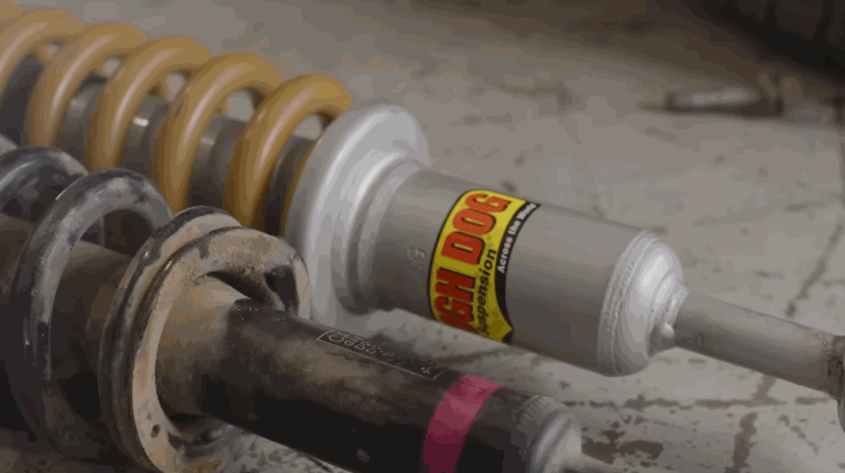 A person wearing gloves is removing a bushing as part of the lift kit installation process on a vehicle's suspension system.