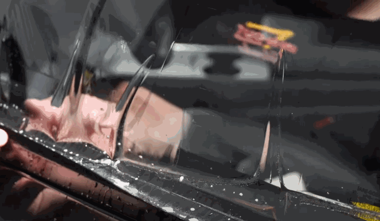 A technician uses a yellow squeegee to smooth out water and air bubbles under a freshly applied tint film.
