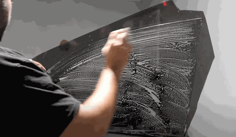 A technician scrubs a car window with soapy solution to remove dirt and residue before applying tint film.