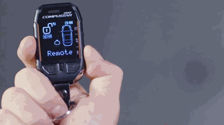 A hand holding a Compustar key fob displaying a remote start interface with a car diagram and the word “Remote”.