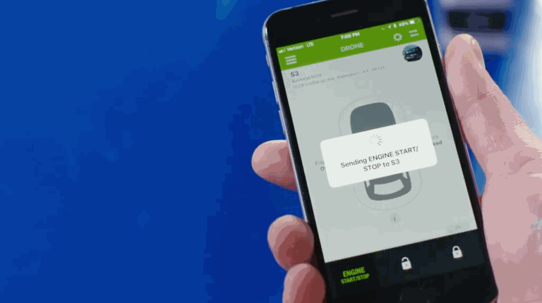 A hand holding a smartphone using a remote start app to send an engine start command to a vehicle.