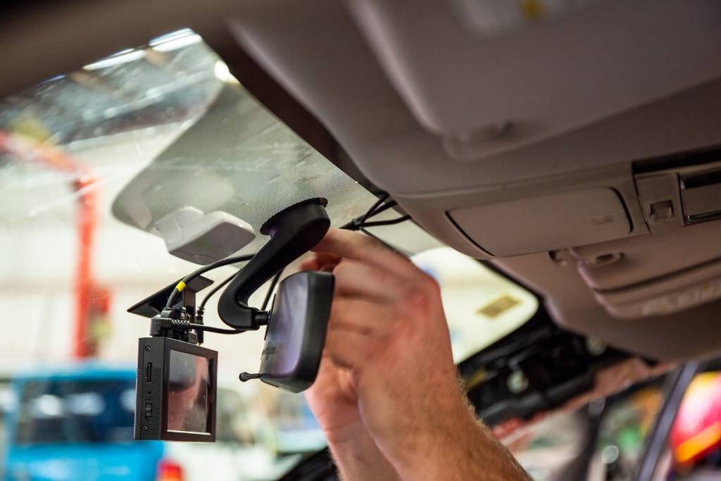 A technician installing and wiring a dash cam on a car windshield near the rearview mirror.