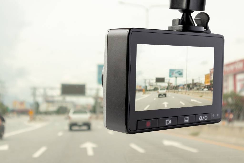 A dash cam mounted on a car windshield recording vehicles on a multi-lane road.