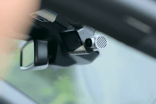 A person installing a compact dash cam on a car windshield near the rearview mirror.