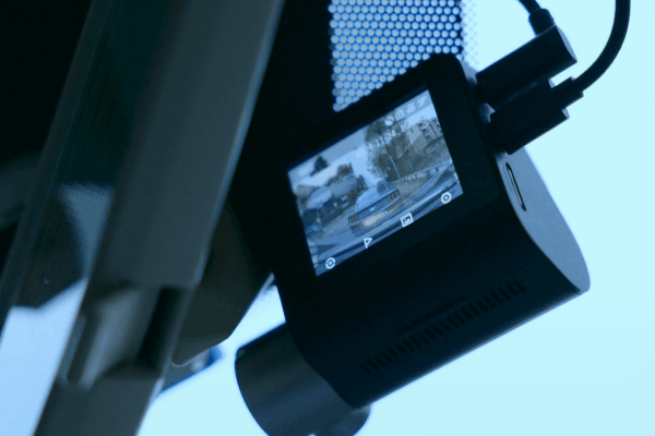 A person adjusting a dash cam screen showing recorded footage of cars on the road.