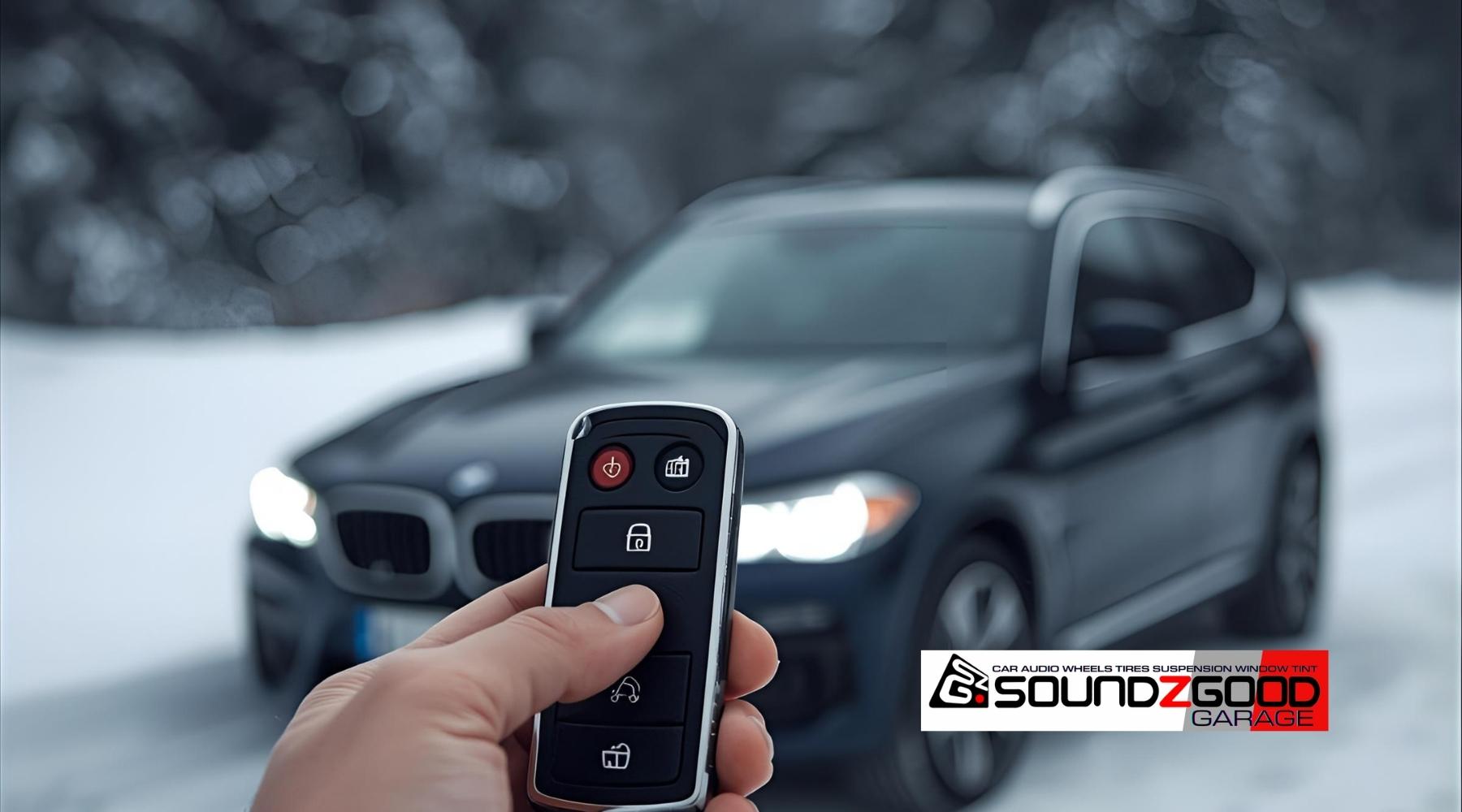 Hand holding a remote car starter in front of a black vehicle warming up on a snowy morning, with Soundz Good Garage logo in the corner.