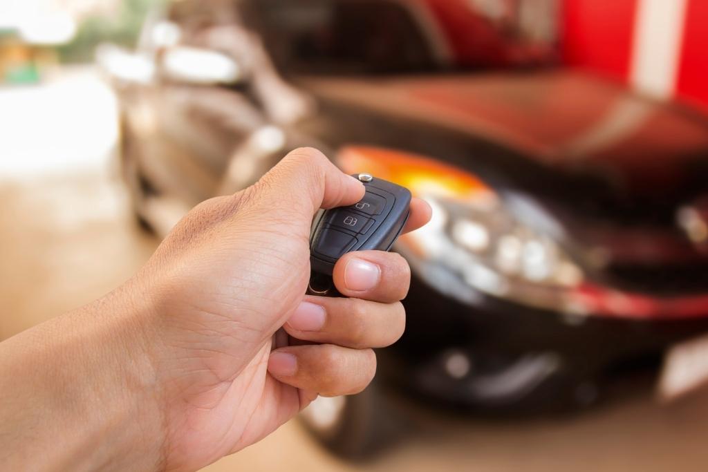 Close-up of a person using a car remote to start or unlock a black vehicle parked in a garage.