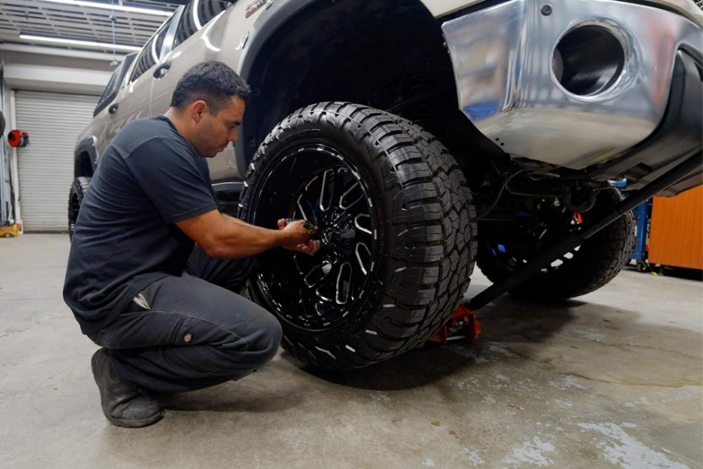Technician installing black custom off-road wheels on a lifted truck at an auto shop