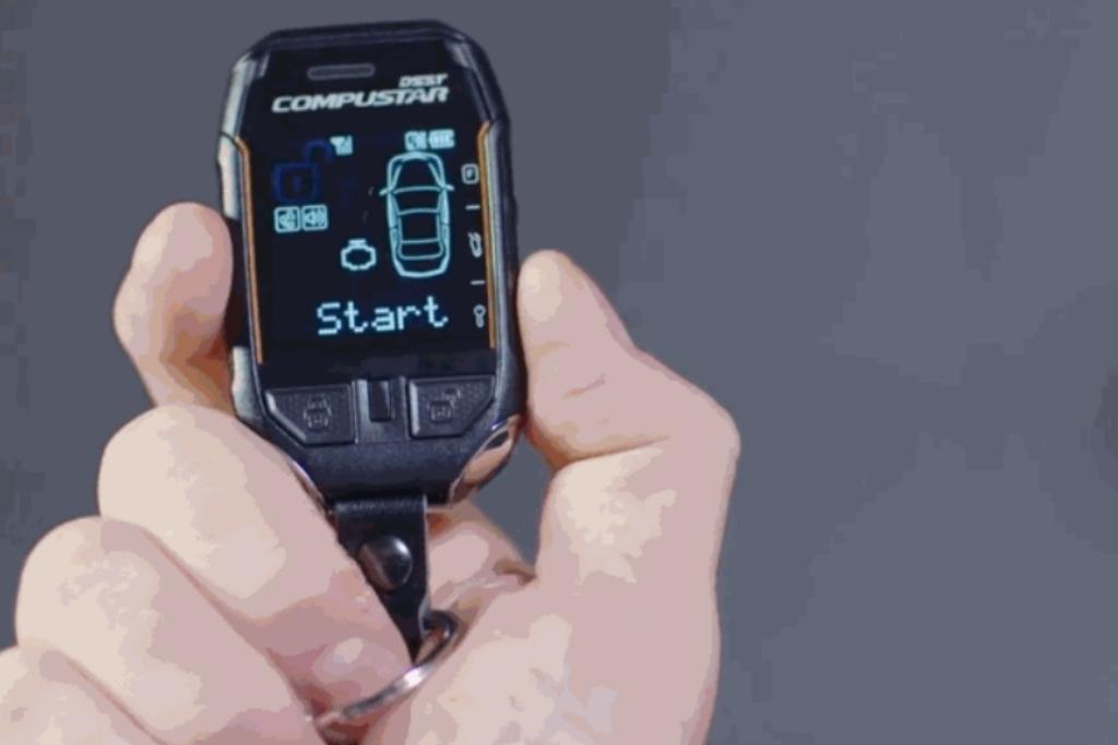 Close-up of a hand holding a Compustar remote car starter with a digital display showing "Start" and a vehicle diagram.