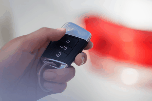 Close-up of a hand holding a modern car remote key fob with lock, unlock, and trunk buttons visible.