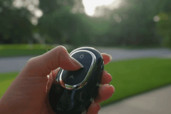 Close-up of a person pressing a button on a sleek remote starter key fob outdoors.