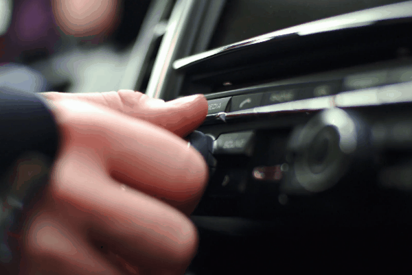Close-up of a factory car stereo system being adjusted by a driver, highlighting standard media controls.