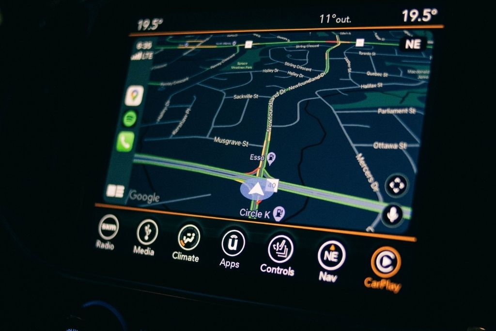 Close-up of a car's dashboard touchscreen displaying Apple CarPlay navigation with Google Maps, showing route guidance and nearby locations.
