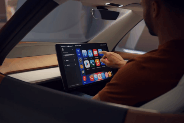 Driver using a large touchscreen infotainment system with Apple CarPlay and Android Auto apps inside a modern vehicle interior.