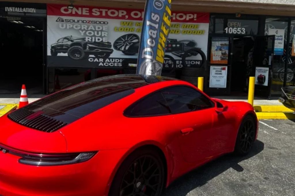 Red sports car parked outside Soundz Good Garage auto customization shop offering car audio, wheels, tires, suspension, and window tint services