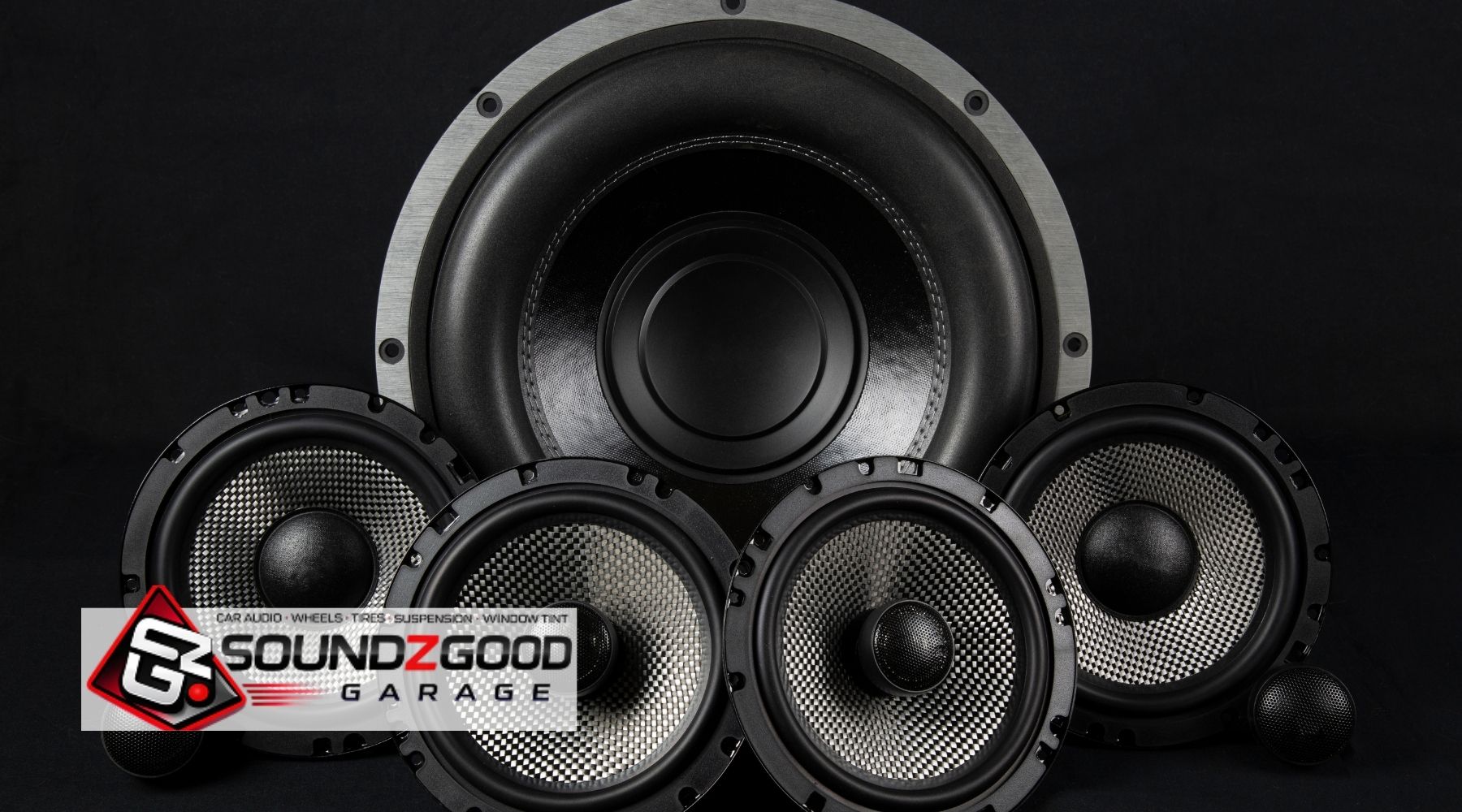 Car audio speakers and subwoofer display with Soundz Good Garage logo on a black background
