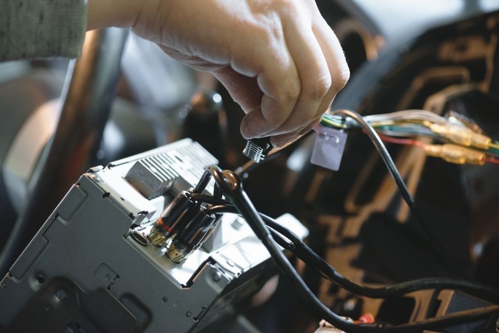 Technician connecting wiring during car stereo installation inside a vehicle dashboard
