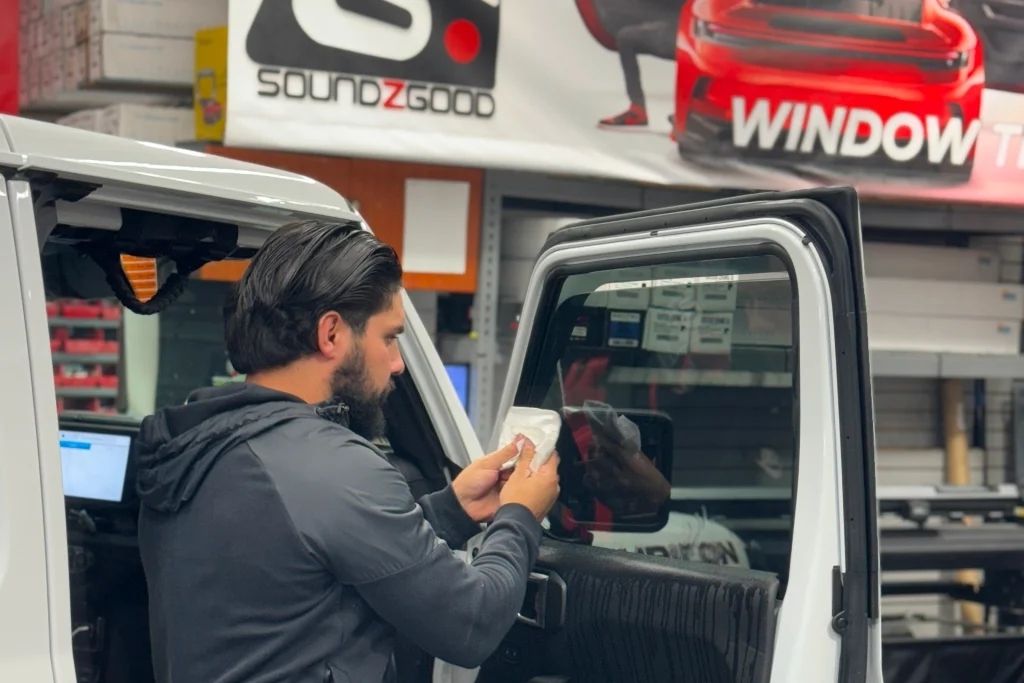 Technician applying window tint to a vehicle door inside Soundz Good Garage shop.