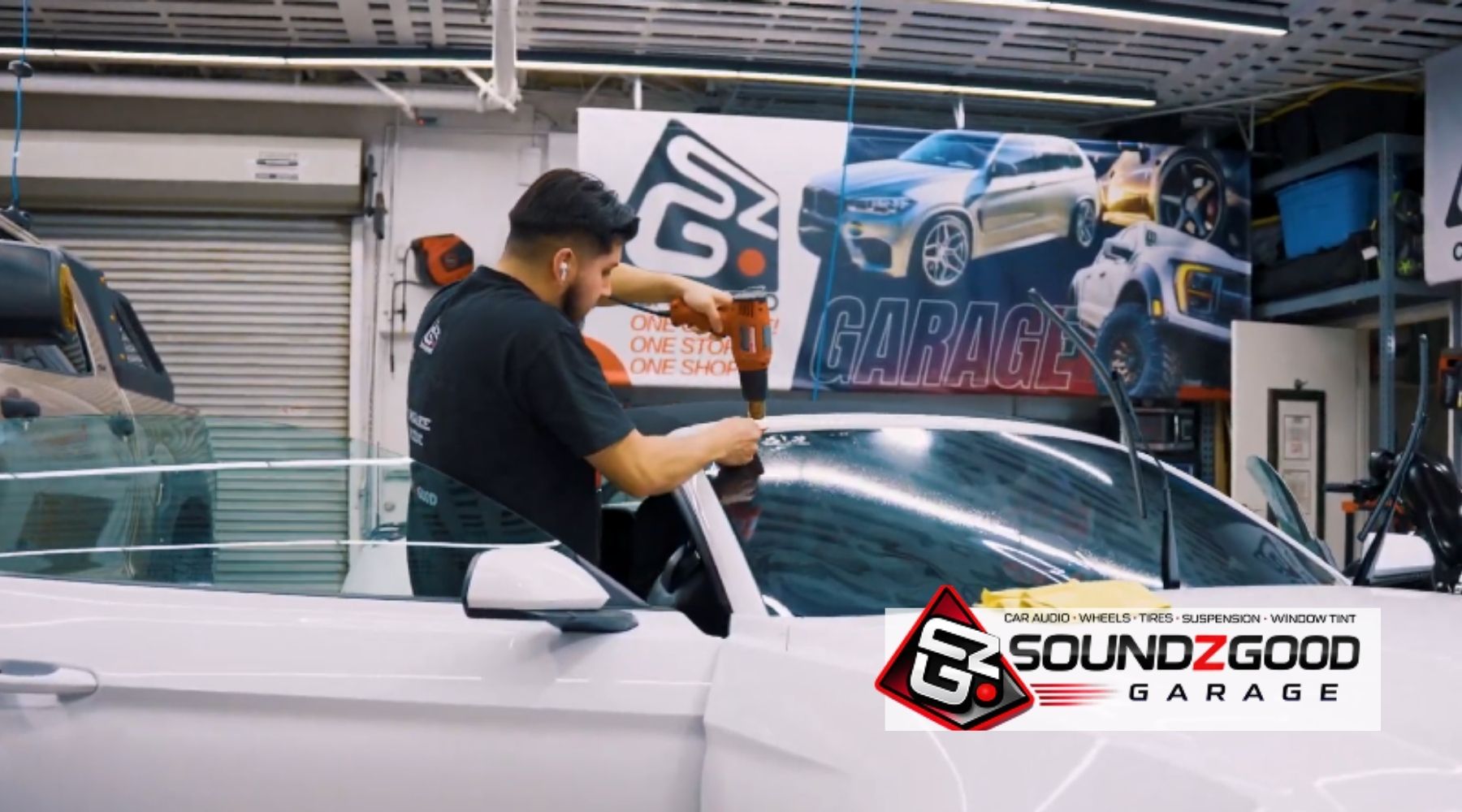 Soundz Good Garage technician installing window film on a white car inside the shop