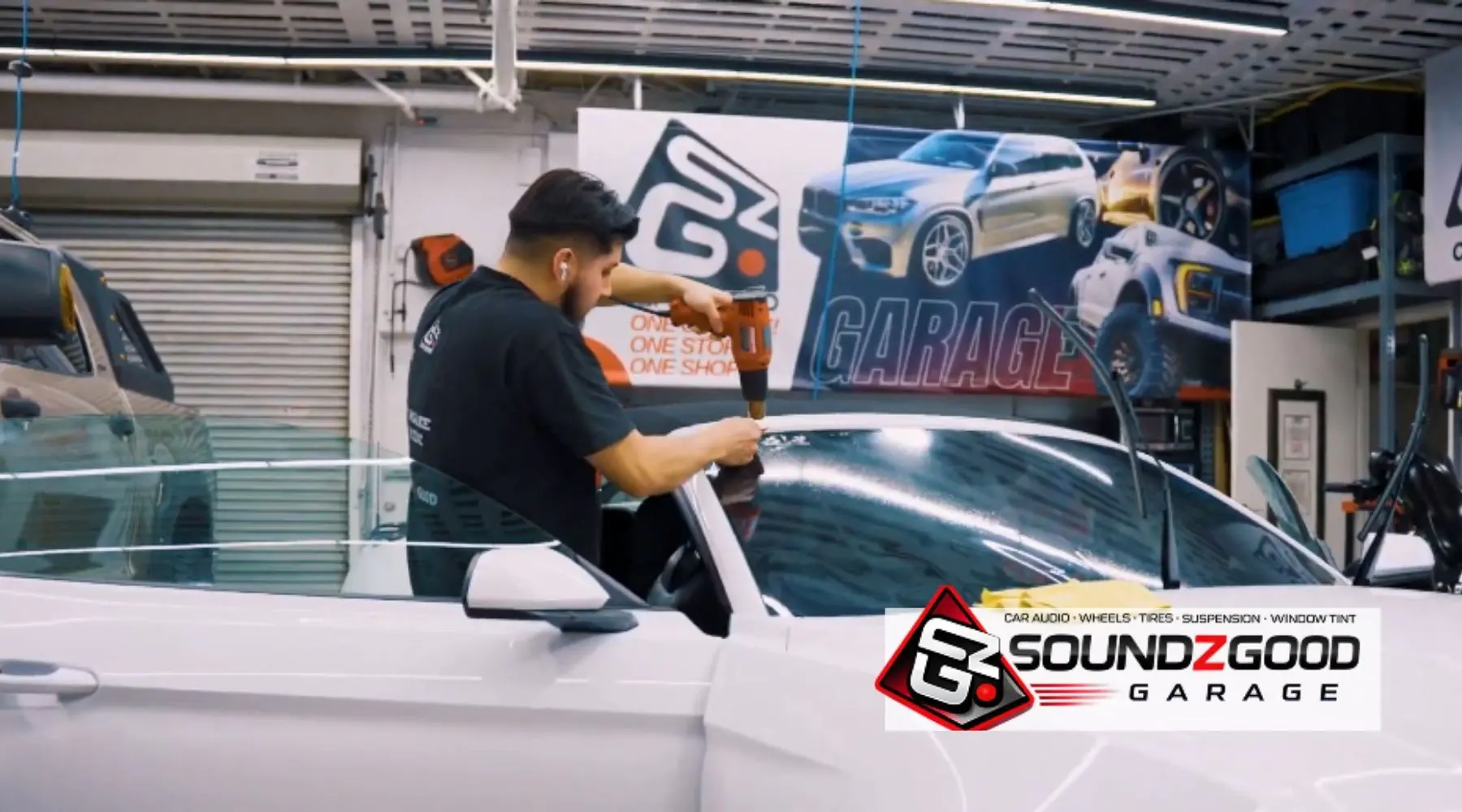 Soundz Good Garage technician installing window film on a white car inside the shop