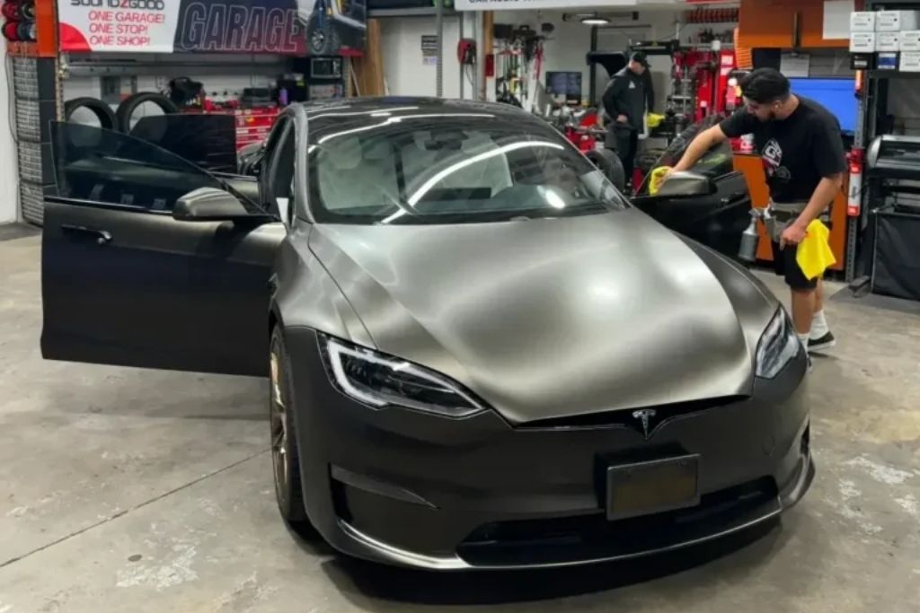 Technician cleaning and preparing a matte black Tesla for professional ceramic window tint installation inside Soundz Good Garage.