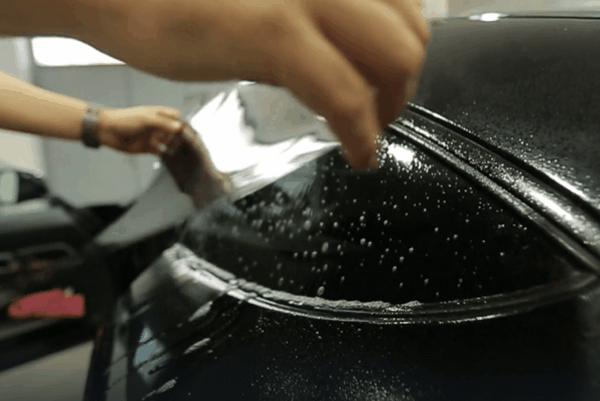 Close-up of a technician applying ceramic window tint film to a vehicle window during professional installation.