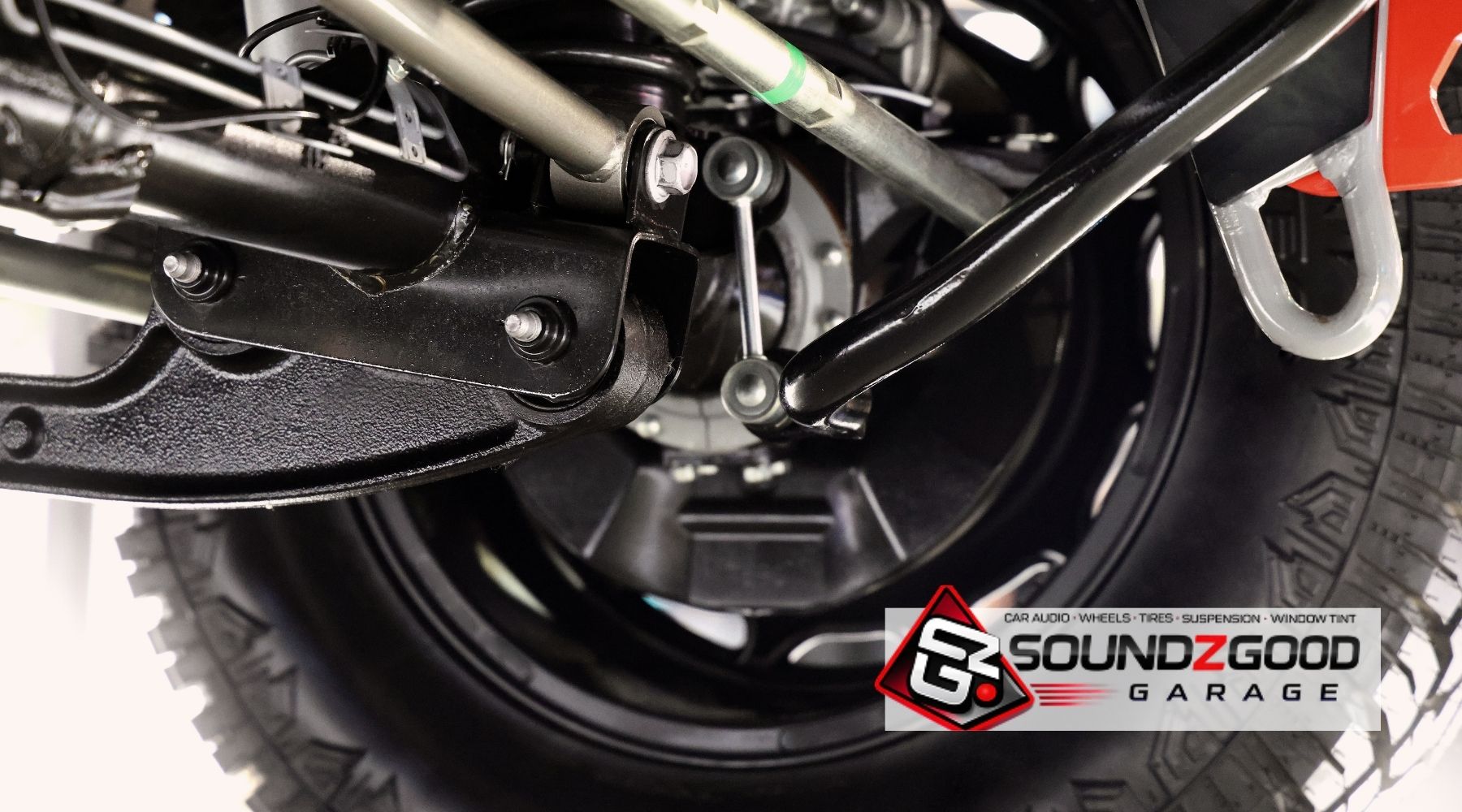 Close-up of vehicle suspension components and tire with Soundz Good Garage branding.