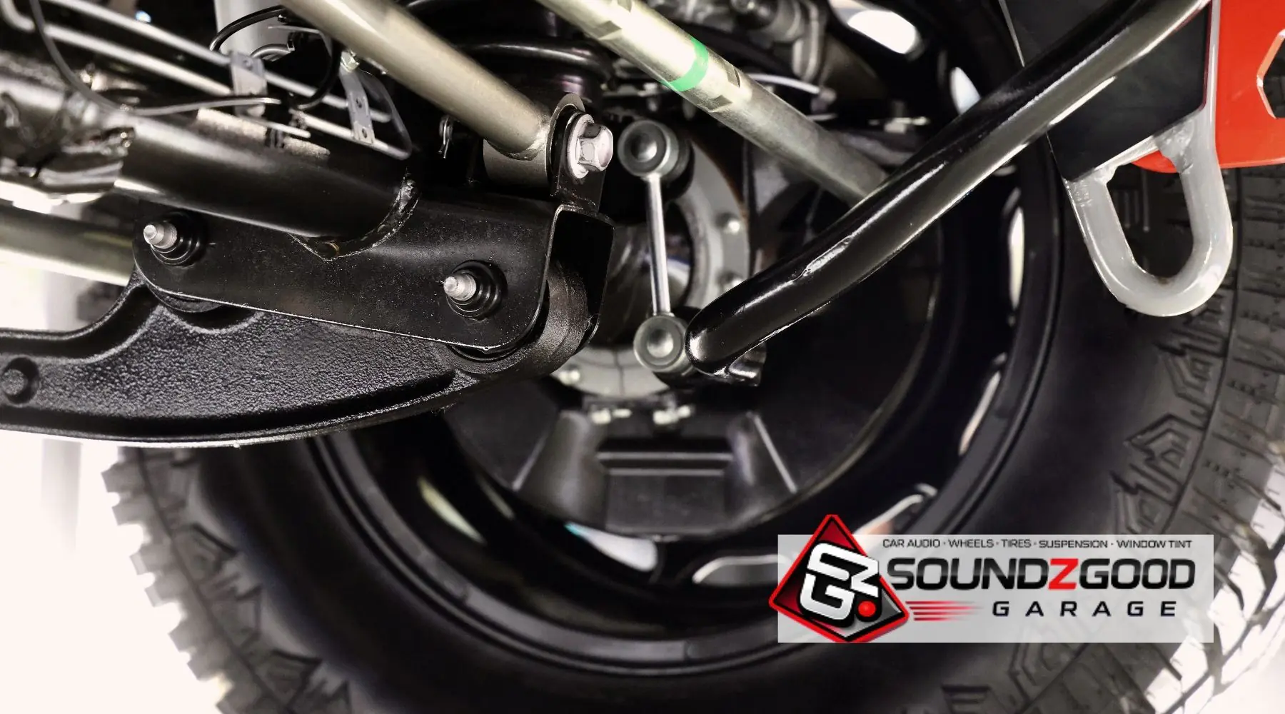 Close-up of vehicle suspension components and tire with Soundz Good Garage branding.