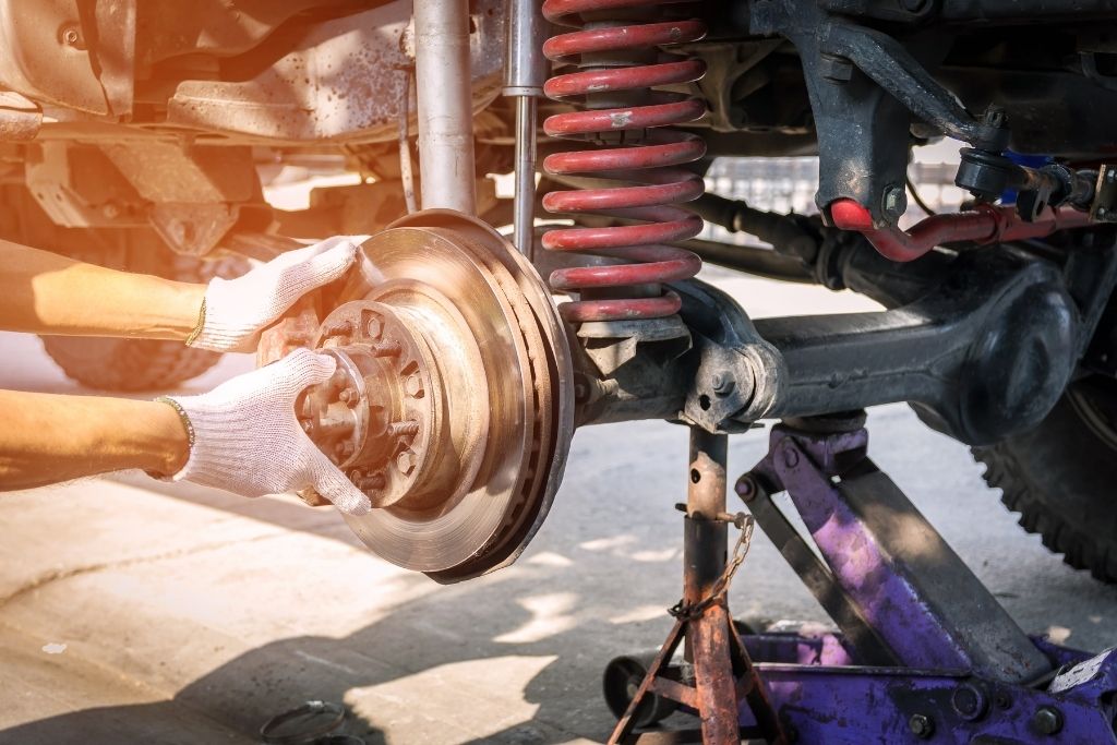Technician inspecting vehicle suspension and brake assembly with red coil spring during suspension service