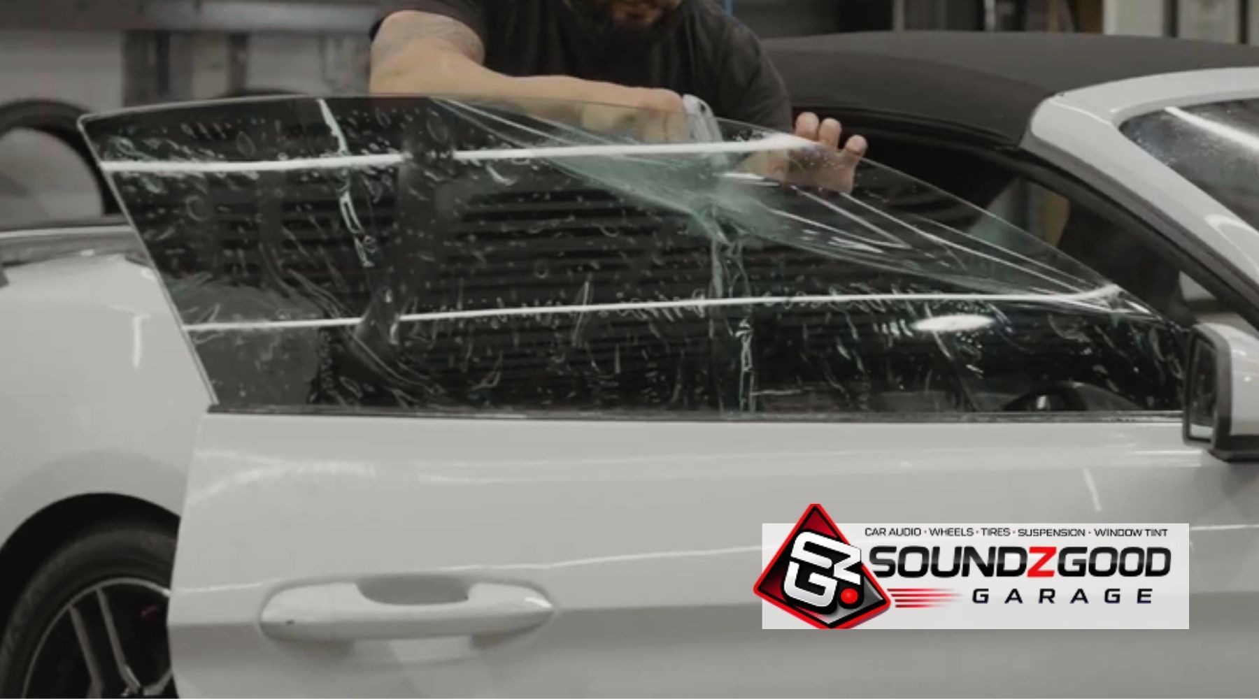 Technician applying window tint film to the side window of a white convertible at Soundz Good Garage.