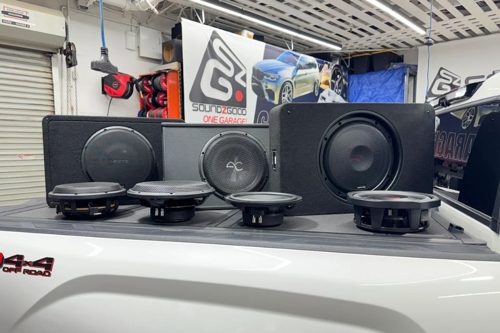 Car speakers and subwoofers displayed on a truck bed inside the Soundz Good Garage workshop.