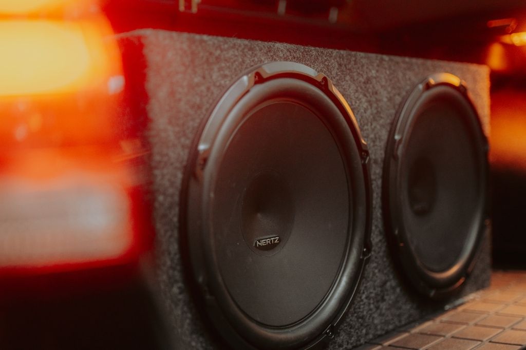 Two Hertz subwoofers installed in a carpeted enclosure inside a vehicle’s cargo area.
