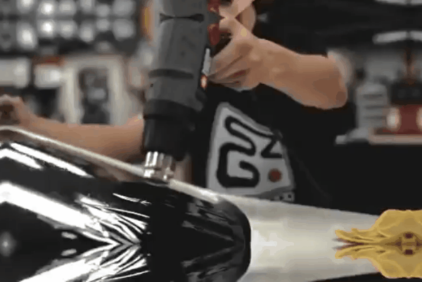 Technician using a heat gun to shape window tint film on a curved car window.