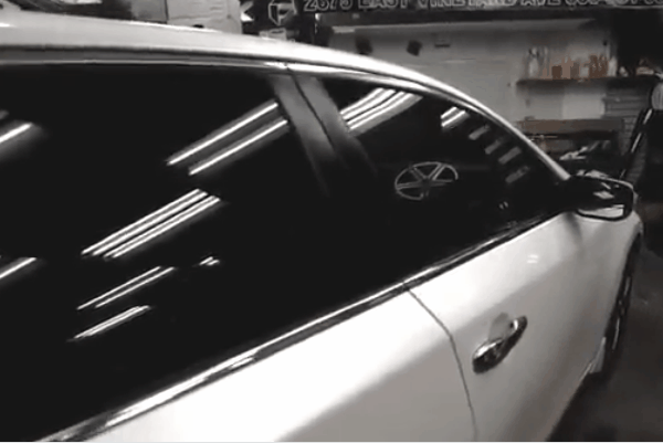 White car with professionally tinted side windows inside an automotive workshop.