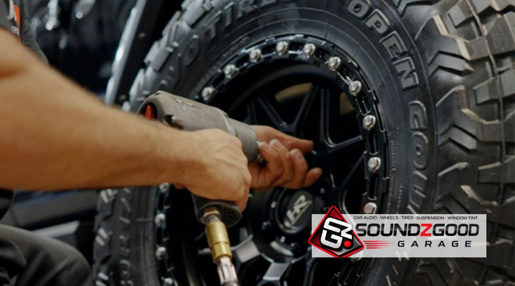 Technician installing a rugged all-terrain tire and black wheel at Soundz Good Garage.