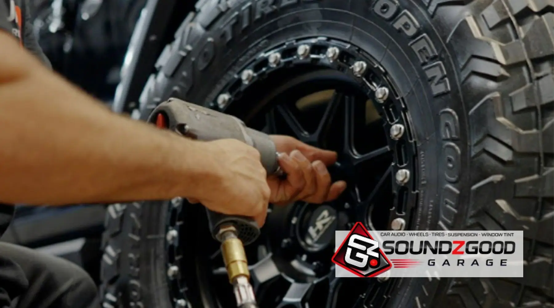 Technician installing a rugged all-terrain tire and black wheel at Soundz Good Garage.