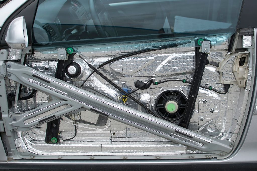 Exposed car door with sound damping material installed around the speaker and inner metal panels for noise and vibration control.