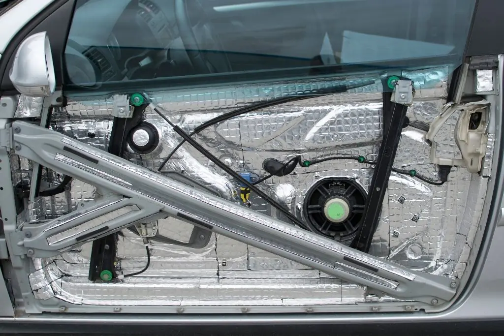 Exposed car door with sound damping material installed around the speaker and inner metal panels for noise and vibration control.
