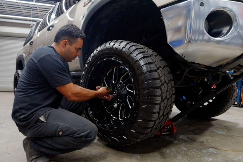 Technician installing a black custom wheel with an all-terrain tire on a lifted pickup truck.
