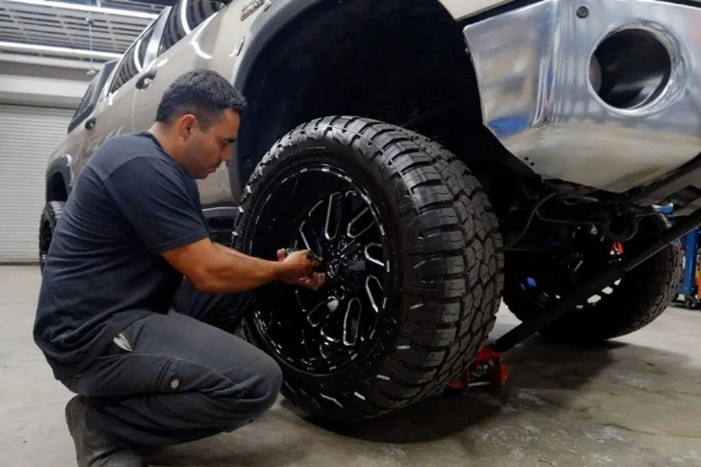 Technician installing a black custom wheel with an all-terrain tire on a lifted pickup truck.