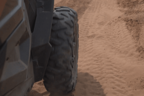 Close-up of an off-road tire driving across loose sand and leaving visible tread marks.